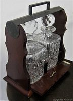 Twin crystal decanter bottles with faceted stoppers nestled inside the wooden tantalus with drop-down front latch open and key placed on the base.
