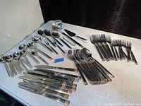 Photo showing knives, spoons, and forks arranged on a table displaying handle design details and quantity.