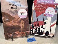 Photo showing both books standing upright with visible covers and price stickers. Wuthering Heights cover depicts a rugged landscape and The Communist Manifesto shows stylized revolutionary figures.