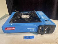 Blue Coleman Camp Bistro butane stove front view showing control knob, burner, and brand logo.
