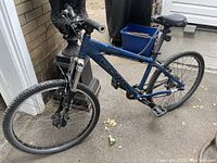 Full side view of the blue Kona Shred trail bike showing the frame, tires, seat, and pedals on a concrete surface outdoors.