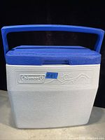 Front view of Coleman cooler showing blue lid, white body with embossed logo and design