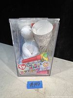 Front view of the unopened TY Color Me Beanie Birthday Kit showing white beanie figure, coloring crayons, and paper cone inside clear plastic box.