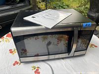 Full view of the Danby stainless steel microwave placed on a floral tablecloth with the manual on top.