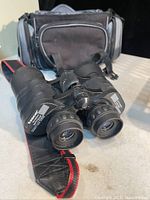 Pair of black Tasco Zip Focus binoculars with lenses facing forward on a surface, showing textured grip and focus wheel, with carrying case behind.
