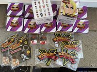 12 boxed Street Fighter V toy figures arranged with patches and keychains on a surface
