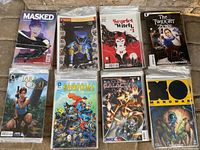 Photo showing eight stacks of comic books with exclusive variant covers including Masked, Power Rangers, Scarlet Witch, The Twilight Zone, Lara Croft, Essential Super Heroes, Battlestar Galactica, and Manowar. Each title has 8 copies.