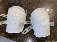 Pair of white plastic kneeling pads with adjustable straps shown on a countertop.