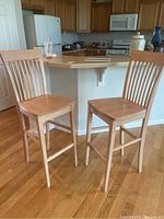 Two wooden bar height chairs with slatted backs and flat seats positioned in kitchen against counter.