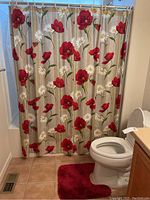 Full view of bathroom corner showing floral shower curtain, red floor rug, white toilet, and beige ceramic tiled floor
