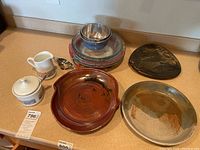 Lot showing four pie plates, small plate carrier, two metal bowls, and three ceramic plates on kitchen counter.