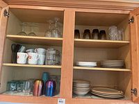 Full cabinet view showing multiple shelves with various glassware and dishware including mugs, glasses, metal tumblers, and plates