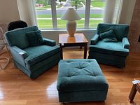 Pair of sea green fabric stationary armchairs with matching square ottoman placed in front of window. Chairs contain matching pillows.