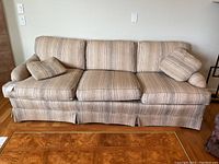 Full front view of the fabric sofa showing three-seat cushions and three back cushions, with two matching pillows on the corners.