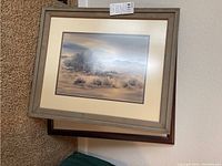 Framed desert landscape artwork in wood frame with muted color palette showing bushes and distant mountains, side view