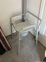 Raised toilet chair with seat closed, showing metal frame and armrests.