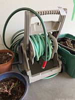 Photo of beige plastic hose caddy with green garden hose coiled on it, showing overall condition and setup.