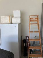 Wooden ladder with 6 steps next to refrigerator that has 3 white styrofoam coolers on top.