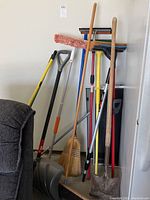 Photo of various brooms, shovels, and mops standing against the wall showing condition and quantity