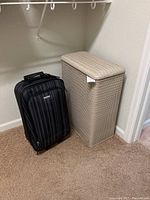 Laundry hamper and travel suitcase shown side by side on carpeted floor.