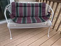 Front view of white metal patio loveseat with striped purple and green cushions on seat, backrest, and armrests.
