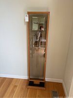 Front view of the tall standing clock with visible glass panel and wooden frame.