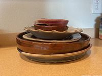 Stack of six ceramic pieces including two small reddish-brown bowls on top, a wavy beige plate, and other rounded plates of varying brown and beige shades.