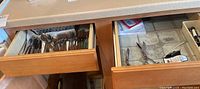 Two kitchen drawers, left drawer filled with flatware (forks, spoons, knives), right drawer with scissors and small utensils.