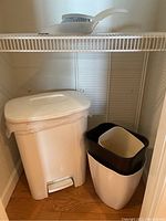 Photo showing the medium-size white pedal-operated waste can and three small nested waste cans on the floor under a wire shelf