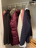 Photo of various women's jackets including black, burgundy with fur hood, white quilted, and navy color.