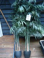 Front view of two artificial palm trees standing side by side with green foliage and black weighted pots.