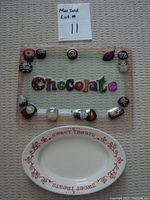 Top-down photo of two plates: one glass chocolate-themed rectangular plate with sweets painted around edge and 'Chocolate' text in center; one oval ceramic plate with red 'Sweet Treats' text around rim.