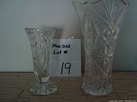 Both vintage crystal vases shown side by side against a wall on a wooden surface with lot number on paper