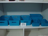 Set of six turquoise plastic storage bins of two different sizes arranged on a white shelf, showing overall condition and color.