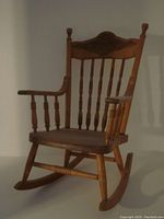 Full view of the antique child's rocking chair showing the turned spindles on the backrest and armrests, as well as the solid wood construction and rocker base.