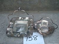 Two-piece antique silver set: square butter dish with handle beside oval bon bon basket with pierced decorative edge and handle