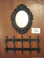 Black oval plastic framed mirror with ornate detailing hung on wood panel wall with two black metal hook racks below