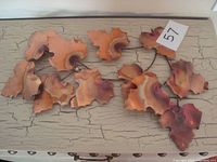 Full view of copper leaf wall art showing multiple copper leaves with hanging hardware on distressed cream colored surface.