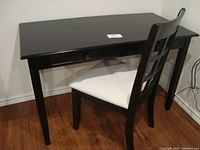 Desk and chair set placed against a wall on a wooden floor, showing desk top, drawer and chair with white seat.