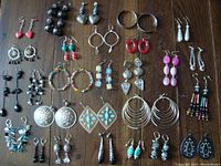 Full view of all 27 pairs of earrings showing various colors, materials, and styles laid out on wooden surface.