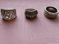 Photo of three Italian sterling silver rings arranged side by side on a pink textured surface. Rings are size 6 with various clear cubic zirconia designs.