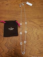 Kate Spade necklace laid out next to the branded soft drawstring pouch on a wood surface.