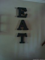 Photo showing three vertically arranged charcoal grey metal letters E, A, T on a wall.