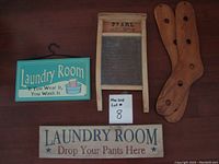 Photo showing two wooden laundry room signs, a PEARL washboard with wood frame and glass surface, and two wooden sock stretchers.