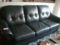 Front view of dark green leather 3-seater sofa showing three seat and back cushions with button tufting