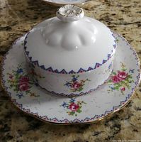 Covered butter dish on matching plate photographed on granite countertop showing petite point floral design and gold trimmed scalloped edge