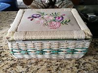 Photo of vintage woven sewing basket with floral embroidered lid showing wear and small stain.