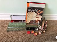 Overview of lot showing cloisonné chopsticks in box, calligraphy set with book, stamps, ink pads, lava beads, and fan.