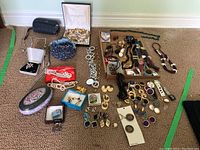 Full assortment of costume jewelry pieces laid out on carpet including earrings, necklaces, watches, brooches, and accessories.