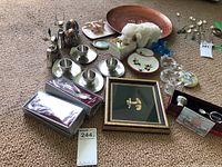 Overview photo of all items in lot on carpet including copper plate, pewter salt bowl and spoon, glass birds, framed artwork, and other decorative pieces